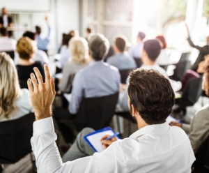 Back of man sitting in a chair raising his hand in a conference